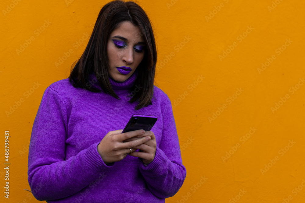 portrait of a woman in purple dress and make-up chatting with a cell phone on a yellow background portrait of a woman in purple dress and make-up chatting with a cell phone on a yellow background