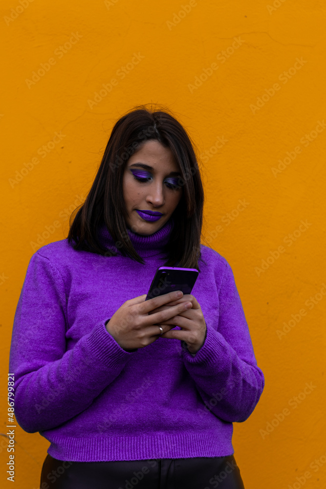 vertical portrait of a woman in purple dress and make-up chatting with a cell phone on a yellow background vertical portrait of a woman in purple dress and make-up chatting with a cell phone on a yellow background