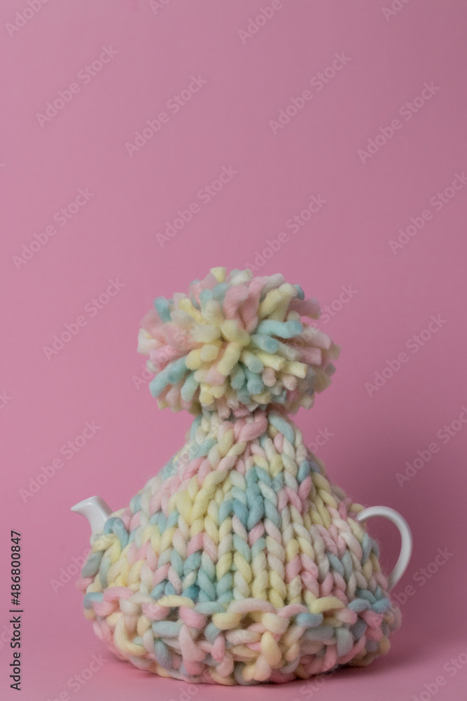 knitted ta cosy on a teapot with pink background 