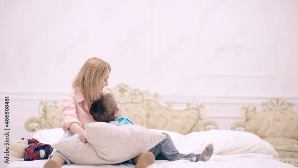 Mom and child son play with pillow in bedroom. Mother with little son playing in the bed at the weekend together, lazy morning. Mom and child son play with pillow in bedroom. Mother with little son playing in the bed at the weekend together, lazy morning.