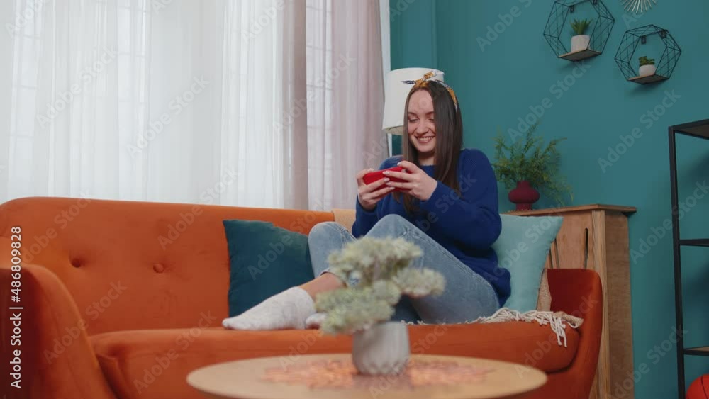 Worried funny addicted woman enthusiastically playing racing video games on mobile phone at home in living room on sofa. Young adult teen girl using smartphone gadget app with drive simulator isolayed Worried funny addicted woman enthusiastically playing racing video games on mobile phone at home in living room on sofa. Young adult teen girl using smartphone gadget app with drive simulator isolayed