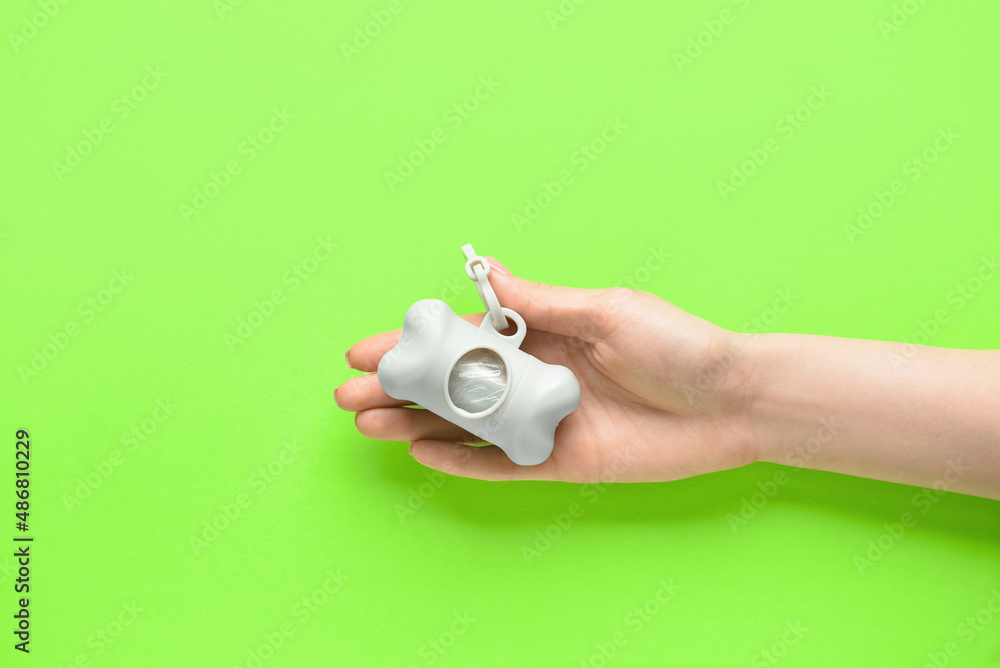 Woman holding dispenser with pet waste bags on green background, closeup Woman holding dispenser with pet waste bags on green background, closeup