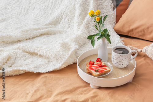 Tray with tasty breakfast and vase with flowers on comfortable bed