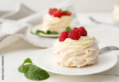Plate of tasty Pavlova cake with fresh berries on light wooden background