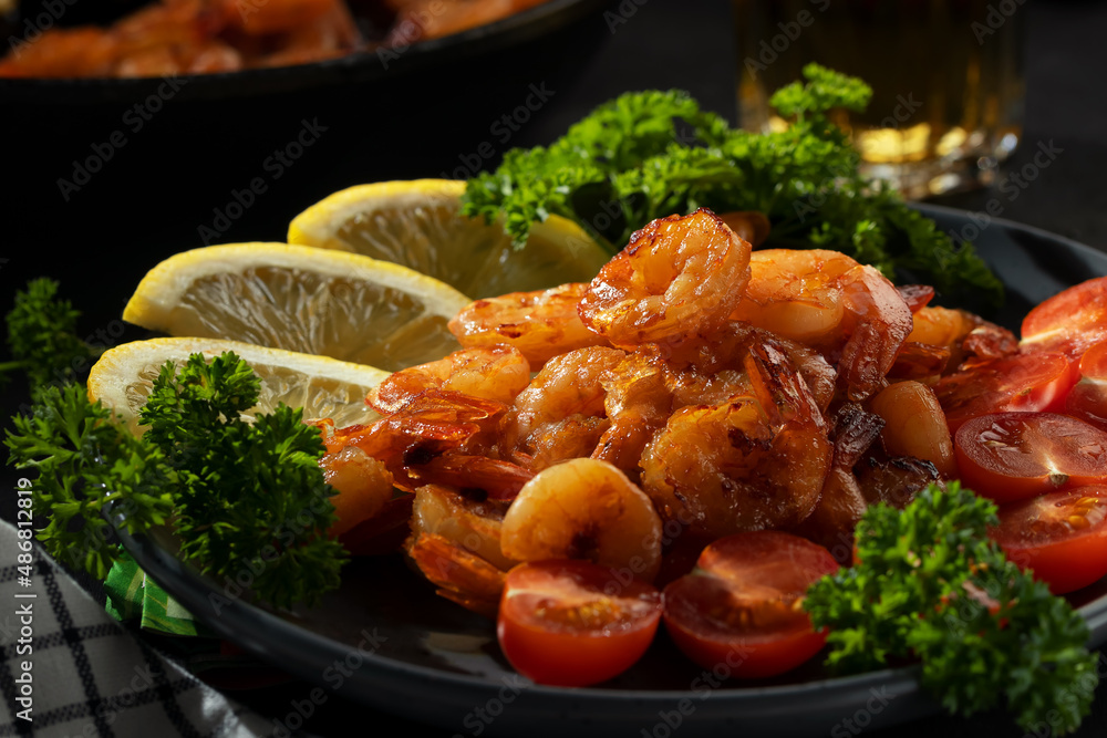 Fototapeta premium Fried shrimps with lemon, tomatoes and herbs on a plate on the table, close up