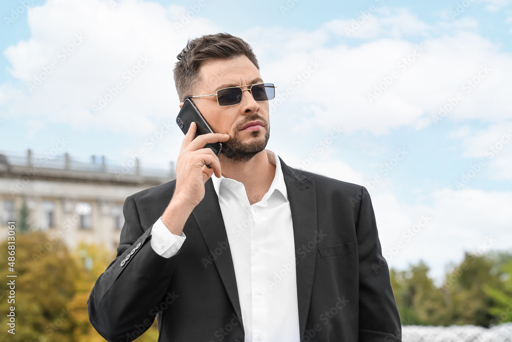 Stylish businessman in sunglasses talking by mobile phone on city square Stylish businessman in sunglasses talking by mobile phone on city square