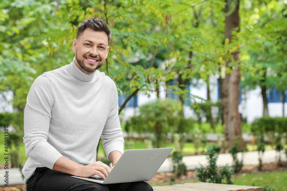 Stylish businessman working with laptop on bench in park Stylish businessman working with laptop on bench in park