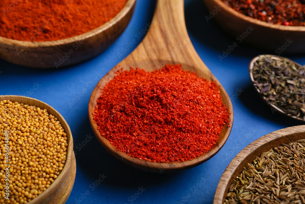 Wooden spoon with red chili powder and different spices on blue background, closeup Wooden spoon with red chili powder and different spices on blue background, closeup