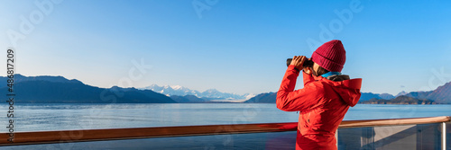 Alaska Glacier Bay cruise ship passenger looking at Alaskan mountains in binoculars exploring Glacier Bay National Park, USA. Woman on travel Inside Passage enjoying view. Vacation adventure banner