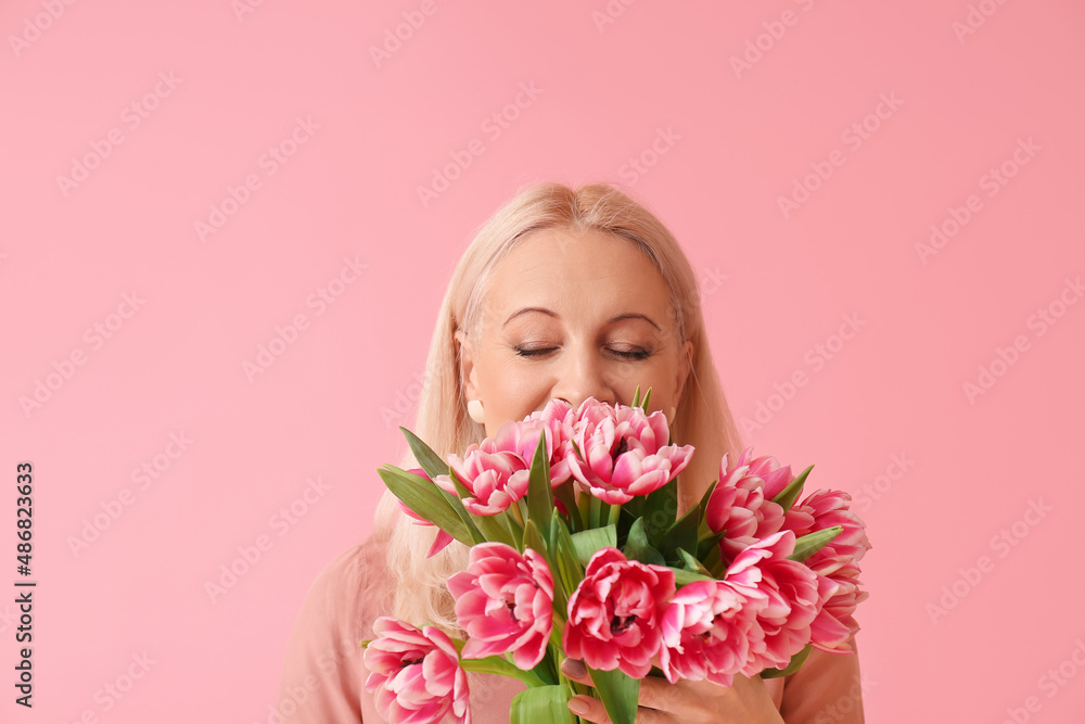 Mature woman with bouquet of tulips on pink background. International Women's Day