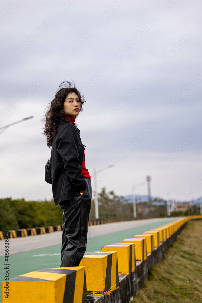 An Asian woman in a black leather coat outdoors