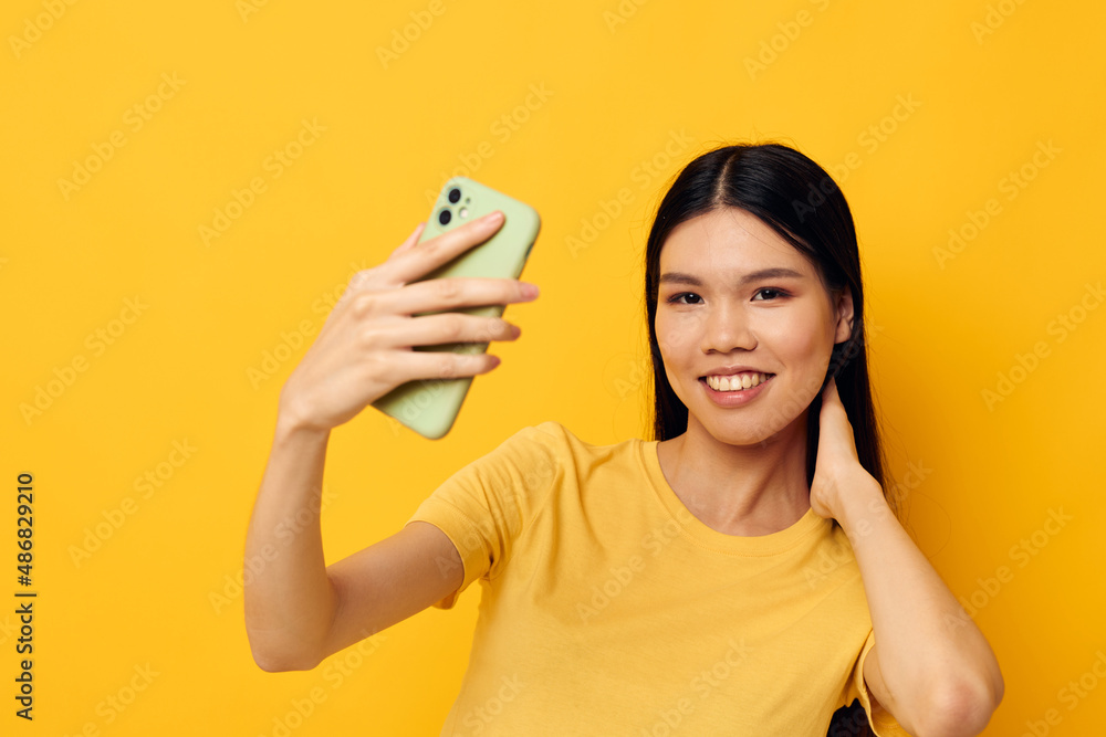 Charming young Asian woman in a yellow t-shirt looking at the phone posing isolated background unaltered Charming young Asian woman in a yellow t-shirt looking at the phone posing isolated background unaltered
