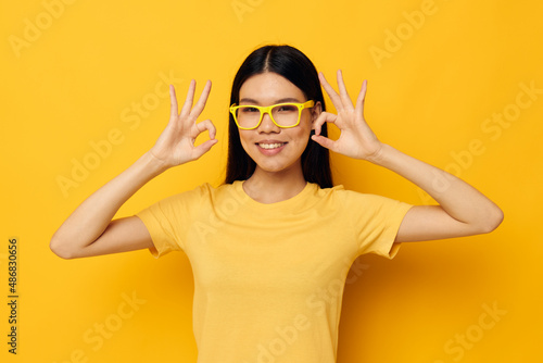 Charming young Asian woman in glasses gesturing with hands copy-space yellow background unaltered