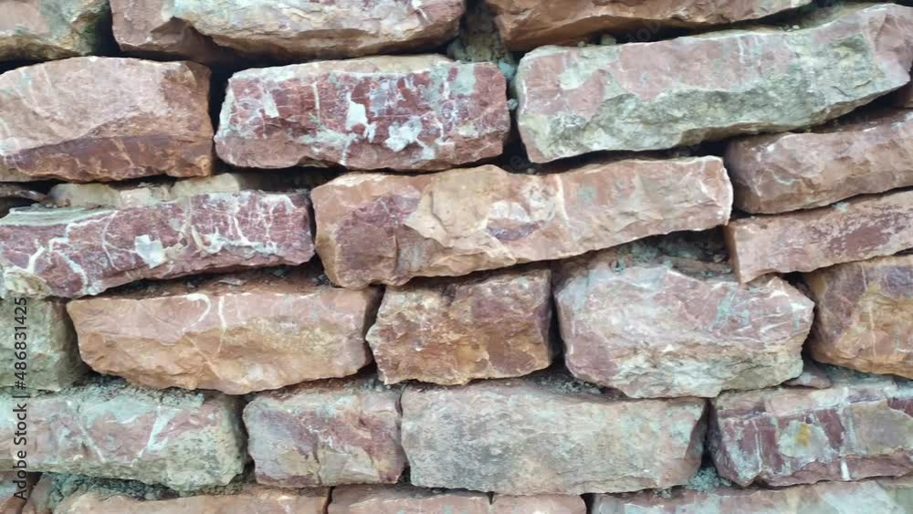 Old stone retaining wall made of irregularly laid blocks of red and pink rock. Pattern and texture of the surface of vintage handmade masonry construction - close up. Old stone retaining wall made of irregularly laid blocks of red and pink rock. Pattern and texture of the surface of vintage handmade masonry construction - close up.