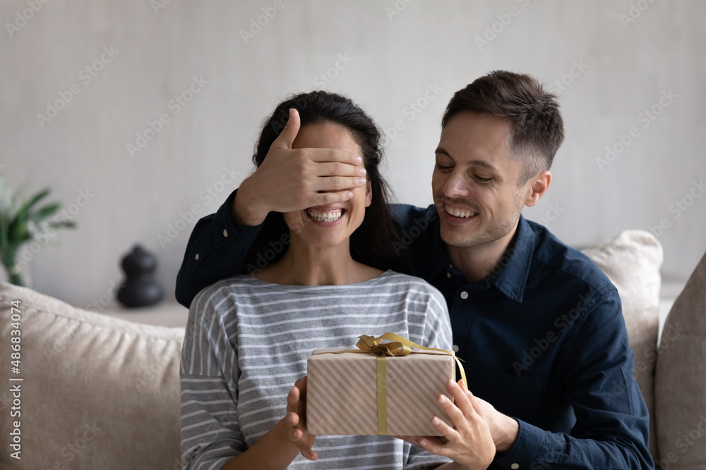 Happy husband giving surprise gift to excited wife. Joyful young man