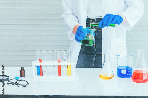 Hand of Scientist in uniform holding beaker and test tube have chemical liquid for testing chemical reaction.