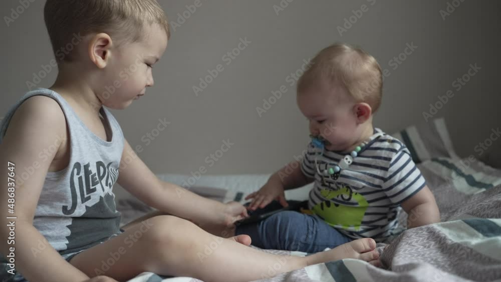 Two brothers (children) play on the bed with a cell phone. Two brothers (children) play on the bed with a cell phone.