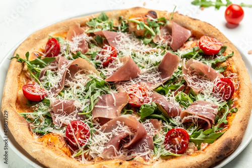 Appetizing italian pizza with cheese, prosciutto, arugula and parmesan. Baked pizza with salami, prosciutto red sauce and cheese. Top view