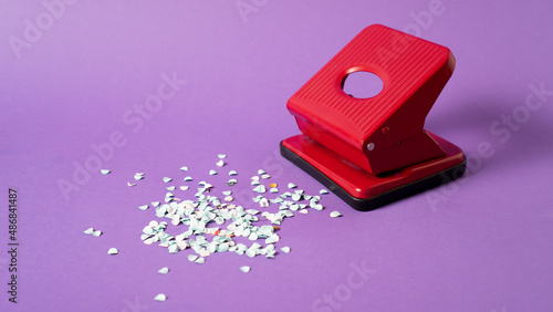 Red confetti maker. Hole puncher machine. Paper punch sprinkle. Hole punch art. Red puncher on violet background photo