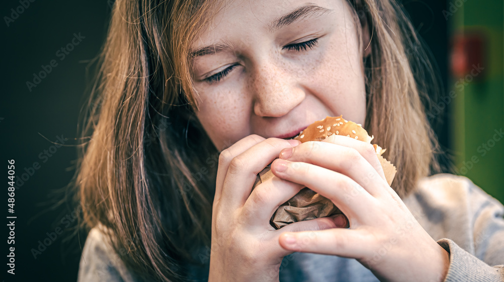A little girl with freckles eats a burger. A little girl with freckles eats a burger.