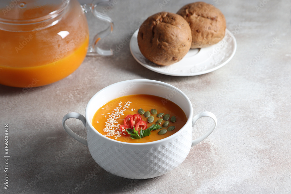 Vegetarian pumpkin soup with herbs in a bowl and homemade rye buns on a gray background Vegetarian pumpkin soup with herbs in a bowl and homemade rye buns on a gray background