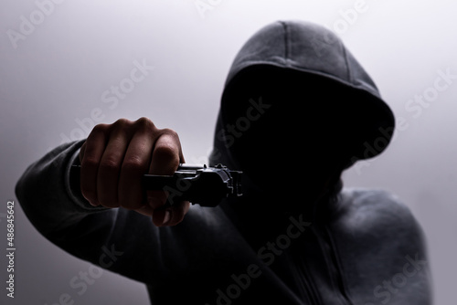 Photo of a creepy horror criminal in black hoodie holding revolver gun. photo