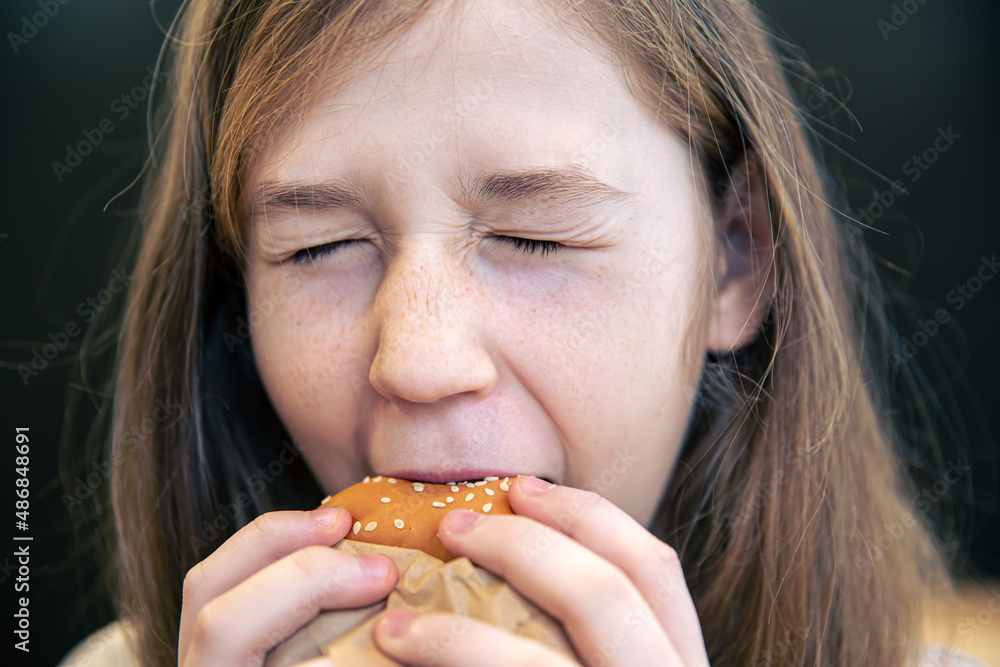 A little girl with freckles eats a burger.