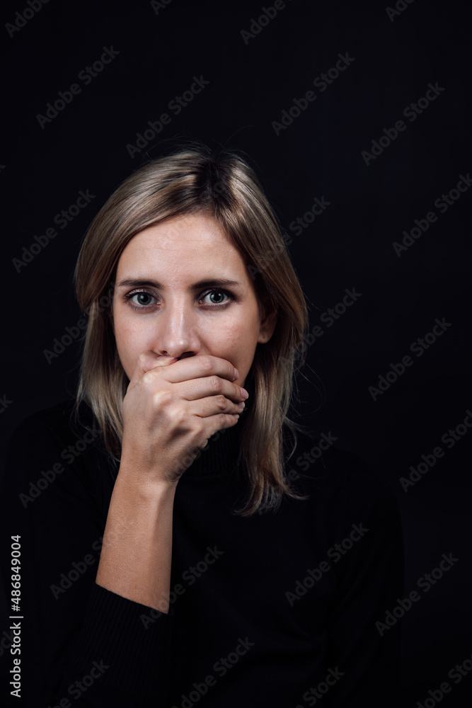 Threatened woman with hand on mouth making her be silent in black blouse on black background. Victim of physical and psychological abuse. Gaslighting. Relative aggression. Threatened woman with hand on mouth making her be silent in black blouse on black background. Victim of physical and psychological abuse. Gaslighting. Relative aggression.