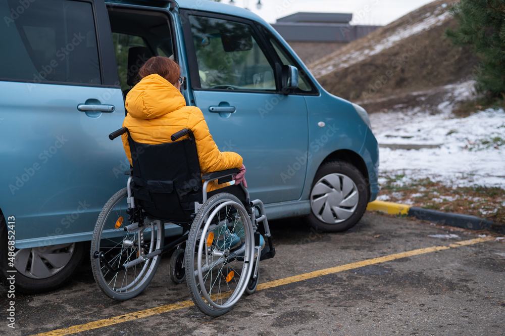 Caucasian woman in a wheelchair gets into the car. 