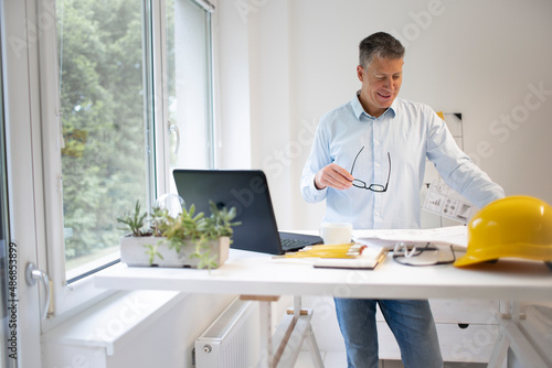 Fotografi Architect with blue shirt is standing at height adjustable work table and is wor