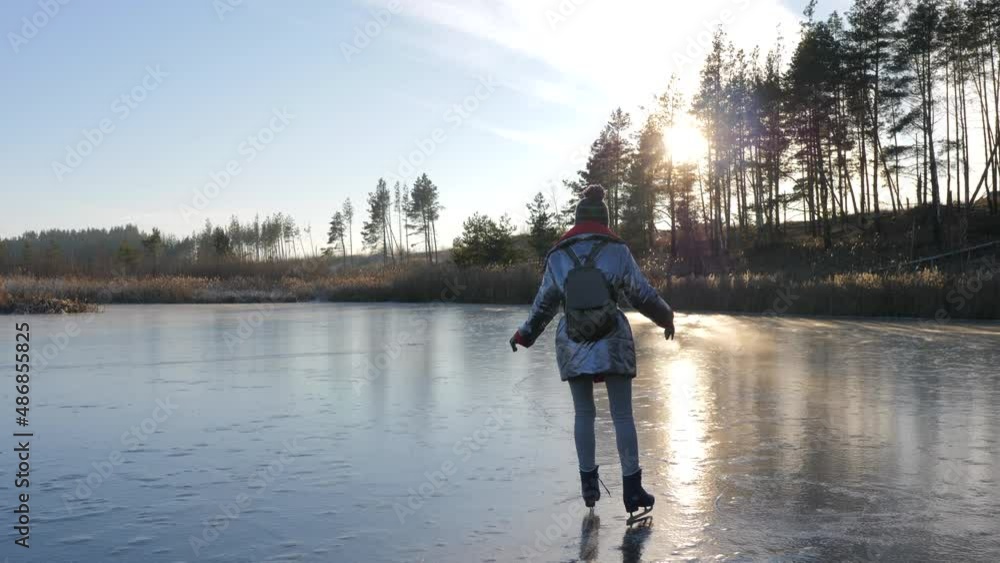 Young girl in a stylish jacket and backpack skates on mirror ice. Rear view. Winter lake with sunny panorama. Young girl in a stylish jacket and backpack skates on mirror ice. Rear view. Winter lake with sunny panorama.