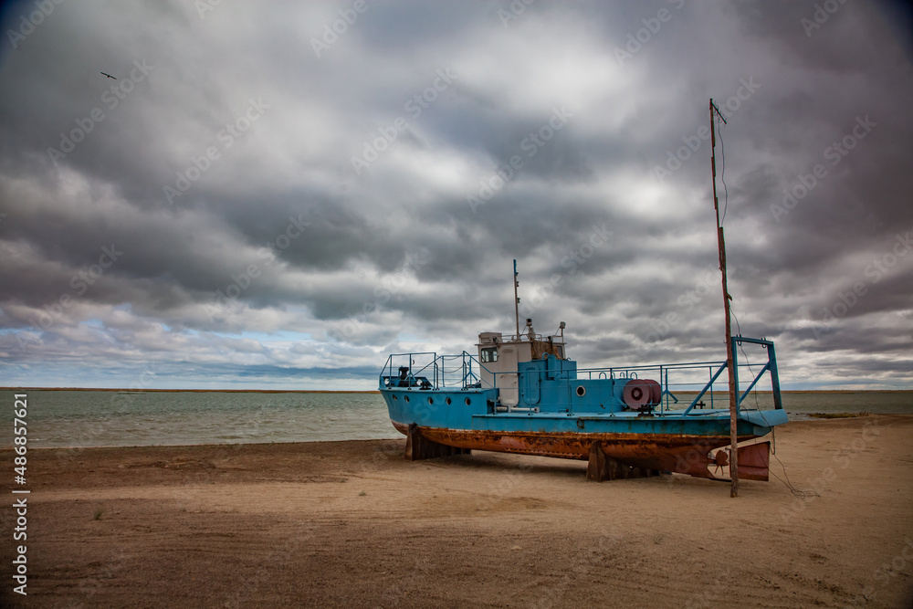 Kok-aral, Kazakhstan - 03 May, 2012: Small Aral sea Kok-aral sand dam. Fishing boat on the beach. Aral on horizon. Grey stormy clouds.