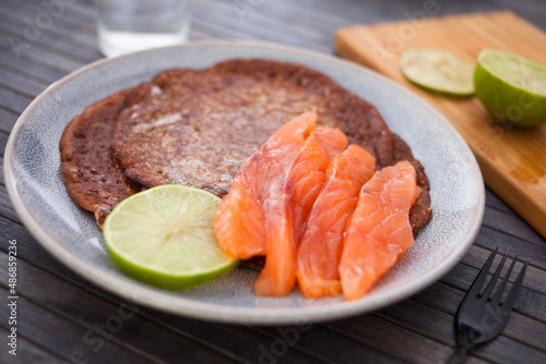healthy breakfast of pieces of salted smoked salmon with buckwheat pancakes and lime