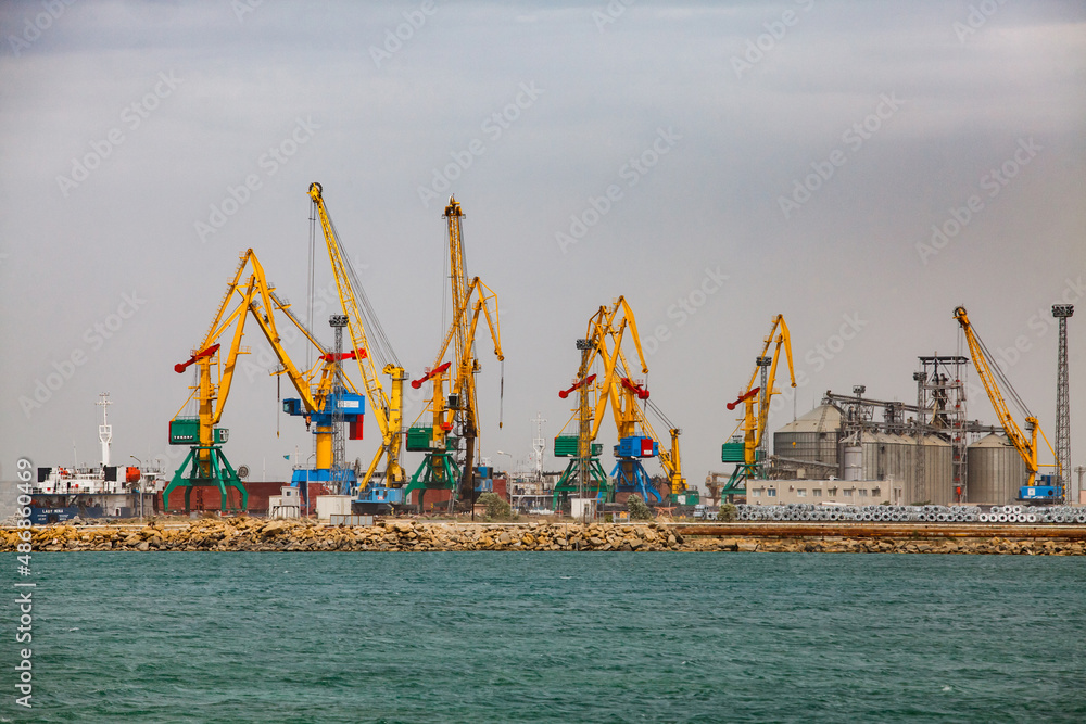 Aktau, Kazakhstan - May 19 2012: Cargo seaport loading terminal on Caspian sea. Yellow dock cargo cranes. Grain elevator right. Grey sky