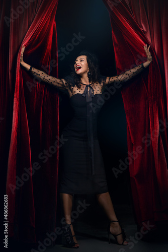 Smiling actress Opening Red Curtain Performing, Woman in Elegant black Dress, on stage, spotlights,