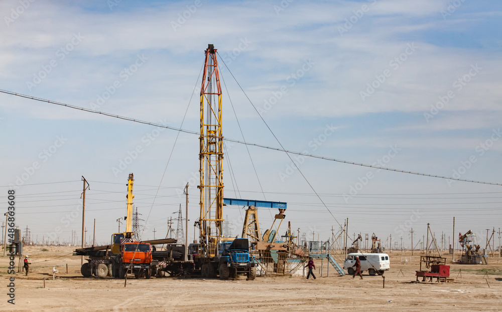 Works on oil drill rig. Workers, auto, trucks and pumping jack in desert. Zhanaozen, Kazakhstan.