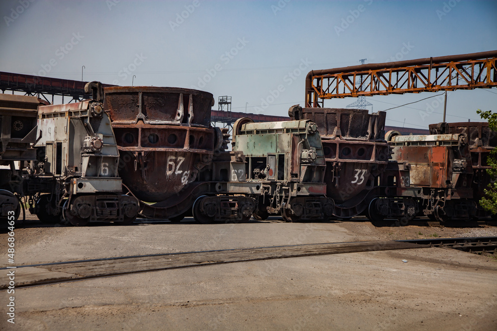 Metallurgical plant (smelter) railroad station. Rusted slag cars on tracks. Blue sky background. Metallurgical plant (smelter) railroad station. Rusted slag cars on tracks. Blue sky background.