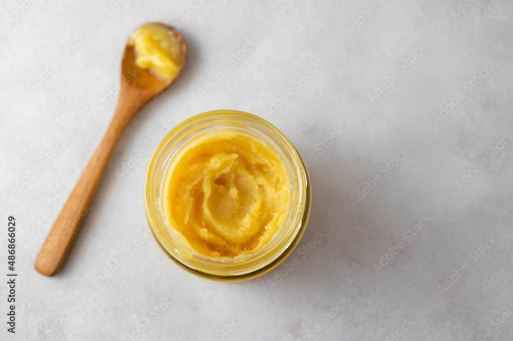 Fototapeta premium Ghee in a glass jar made with sunflower oil on a light background, copy space for text. Hard light.