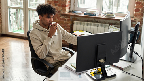 Bilde på lerret Mixed race freelancer or student drinking soda and using multiple screens