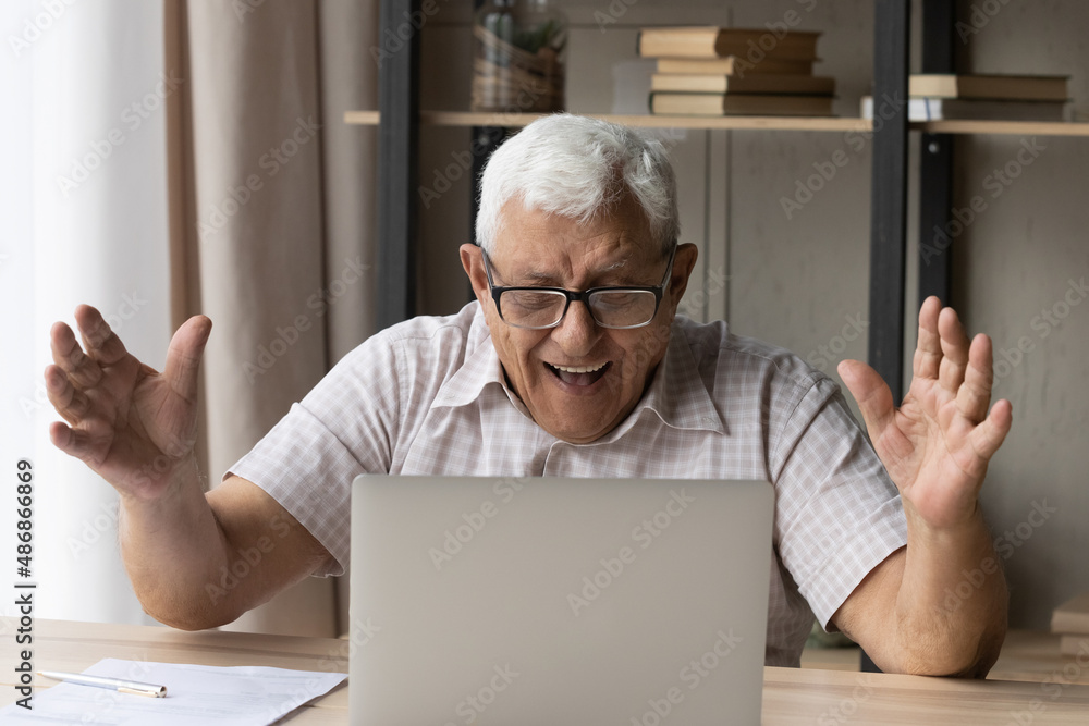 Joyful happy senior 80s retired man excited with good news, receiving email letter, reading message on laptop screen, making surprise, winner gesture, laughing, celebrating success, achieve, luck Joyful happy senior 80s retired man excited with good news, receiving email letter, reading message on laptop screen, making surprise, winner gesture, laughing, celebrating success, achieve, luck