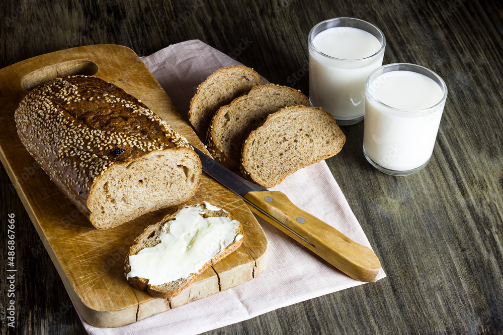 Whole grain bread with sesame on a wooden board. Butter. Milk in glass cups.