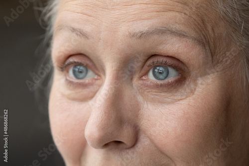 Blue eyes of thoughtful senior 70 woman looking away. Grey haired older lady upper face with natural make up close up. Elderly healthcare, vision, eyesight, eye care concept