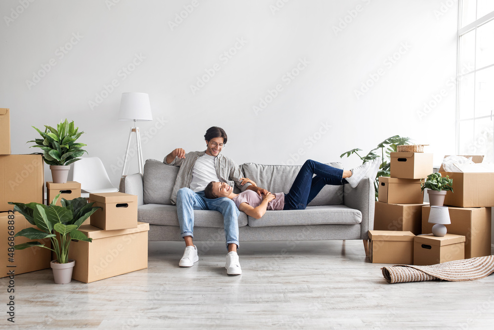 Satisfied caucasian young lady and guy take a break, relaxing on sofa in room interior among boxes with belongings Satisfied caucasian young lady and guy take a break, relaxing on sofa in room interior among boxes with belongings