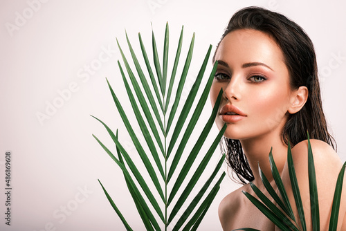 Young beautiful woman with green leaves near face and body. Skin care beauty treatments concept.  Closeup girl's face with green leave. White model with clean, health skin of face - posing at studio
