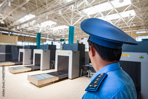 Customs officer in peaked cap and uniform right on foreground, in focus. X-ray apparatus on background, blurred. No passengers.China-Kazakhstan border. Khorgos, Kazakhstan.