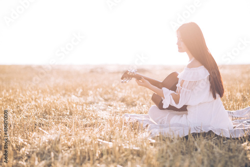 Summer is a great dream time. Beautiful girl playing the guitar in a wheat field