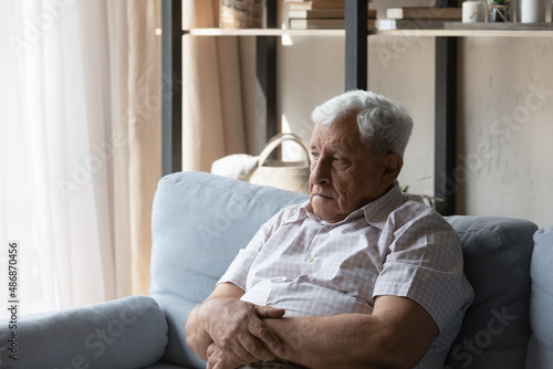 Frustrated senior elder 80s man sitting on sofa at home, looking away, missing family, feeling depressed, lonely, sad, tired, suffering from dementia, Alzheimer disease, memory loss