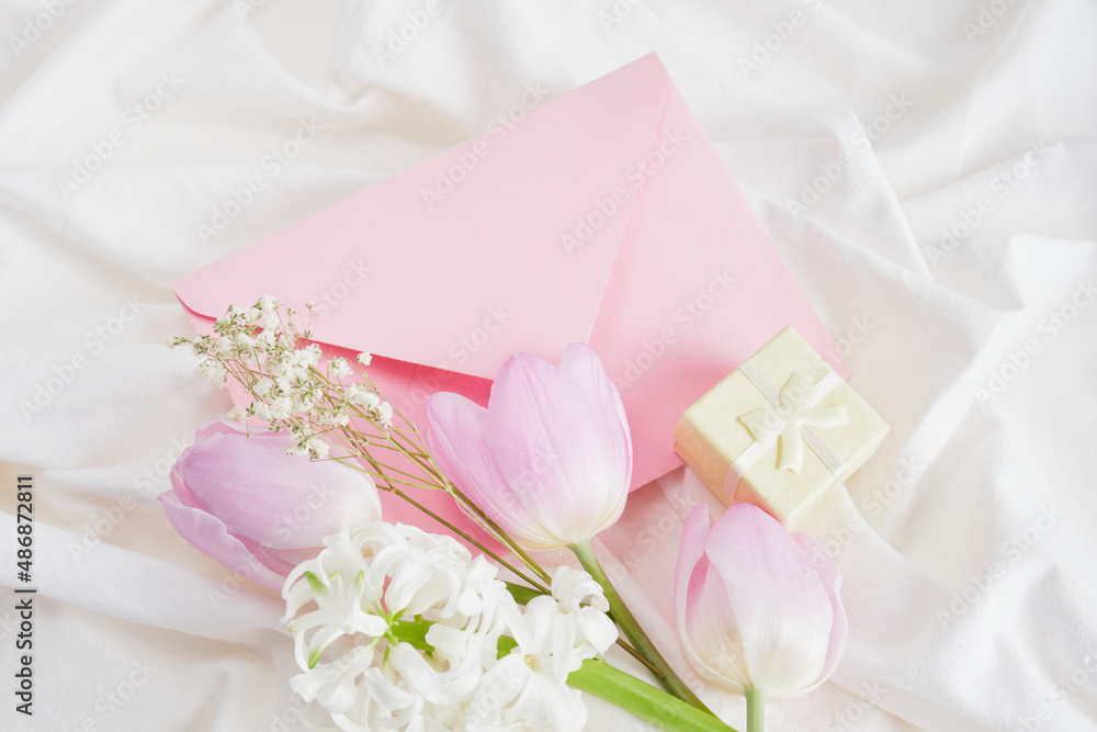 a bouquet of spring flowers in delicate shades, a small yellow gift box and a pink envelope on the bed a bouquet of spring flowers in delicate shades, a small yellow gift box and a pink envelope on the bed
