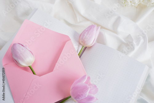 a bouquet of spring flowers in delicate shades, a notebook and a pink envelope on the bed, a romantic gift