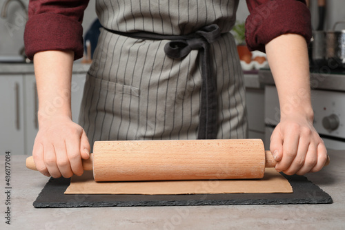 Woman rolling dough with wooden pin at table in kitchen, closeup